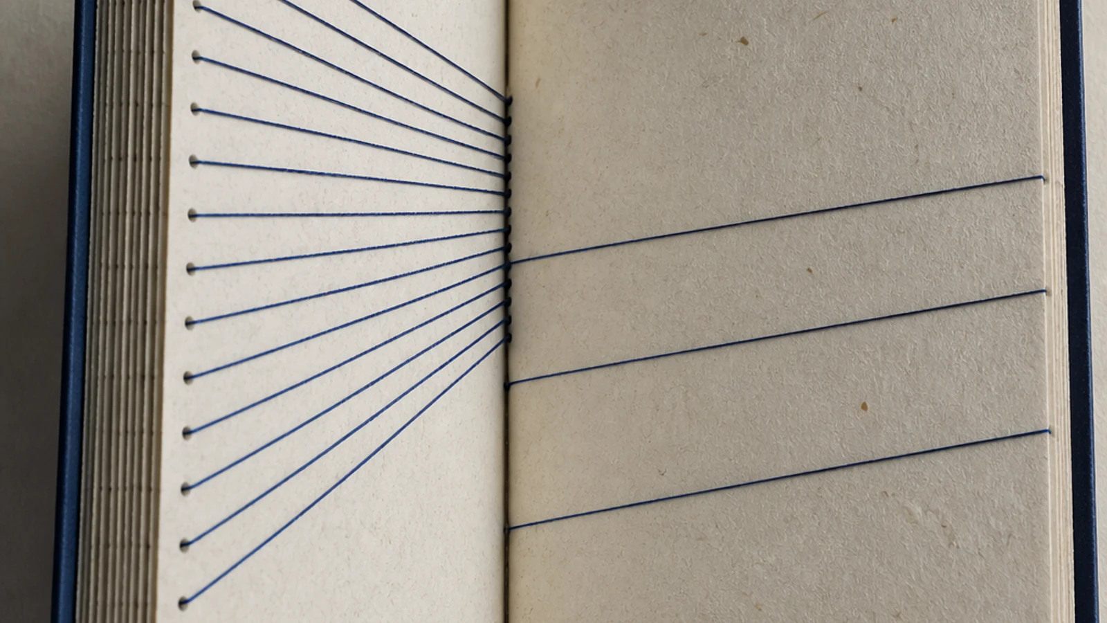 An indigo hand-bound ledger with dense blue threads on one side and sparse threads on the other.