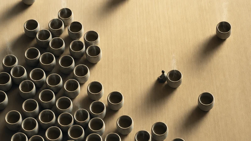 An overhead macro photograph of clustered and solitary yunomi cups on a pale wooden tray, with one miniature seated figure.